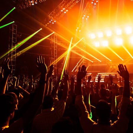 Photo of young people having fun at rock concert, active lifestyle, fans applauding to famous music band, nightlife, dj on the stage in the club, crowd dancing on dancefloor, night perfomance